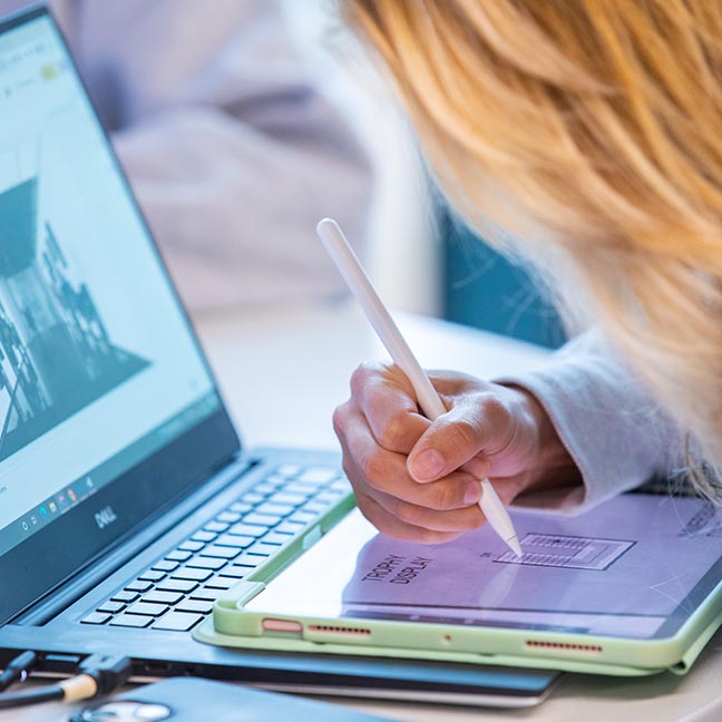 Closeup of a student doing design work on an e-tablet and laptop